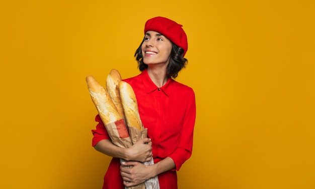 jeune femme française. vêtu d'un costume rouge parisien, tenant du pain français dans ses bras, sourit et regarde de côté.