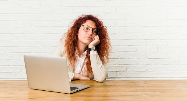 Jeune femme frisée rousse travaillant avec son ordinateur portable qui se sent triste et pensive, regardant l&#39;espace de la copie.