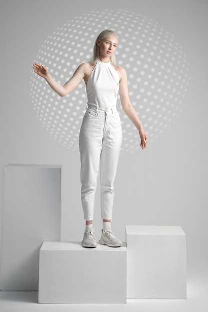 Jeune femme futuriste en vêtements blancs se dresse sur un cube, fond gris clair. Personne de sexe féminin dans un style de réalité virtuelle, technologie future, concept de futurisme, thème cyber ou robot