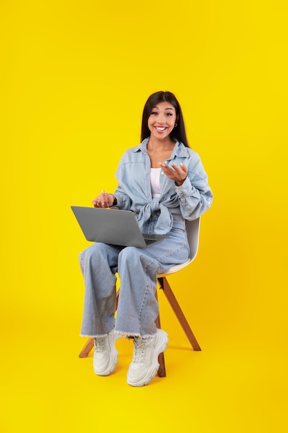 Jeune femme gaie à l'aide de l'ordinateur portable parlant à l'appareil-photo