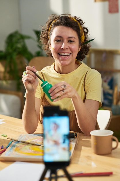 Jeune femme gaie peignant devant un smartphone pendant une masterclass