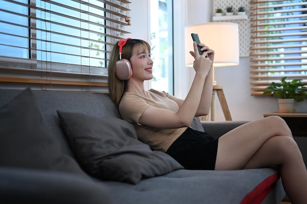 Jeune femme gaie utilisant un téléphone portable tout en se reposant sur un canapé, passant du temps sur Internet sur les réseaux sociaux