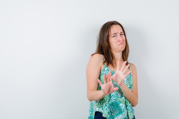 Jeune femme gardant les mains pour se défendre en blouse et ayant l'air effrayée. vue de face.