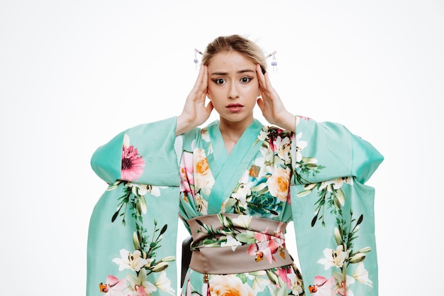 jeune femme geisha en kimono japonais traditionnel, l'air confus et inquiet, tenant la main sur la tête, debout sur un mur blanc