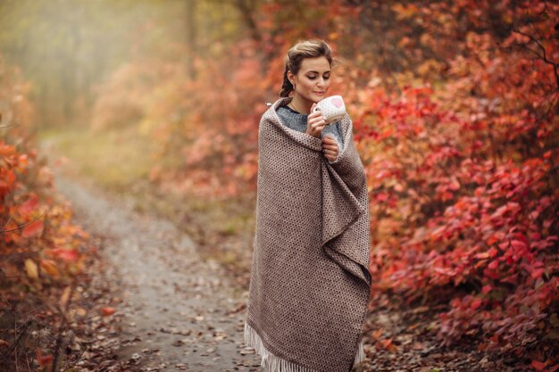 Jeune femme gelée séduisante enveloppée dans un thé à carreaux dans une tasse