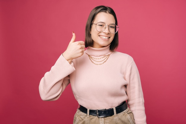 La jeune femme gentille montre le geste de pouce vers le haut tout en souriant à l'appareil-photo