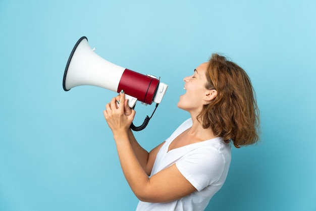 Jeune femme géorgienne isolée sur fond bleu criant à travers un mégaphone pour annoncer quelque chose en position latérale