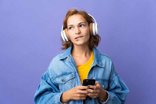 Jeune Femme Géorgienne Isolée Sur Un Mur Violet à L'écoute De La Musique Avec Un Mobile Et De La Pensée