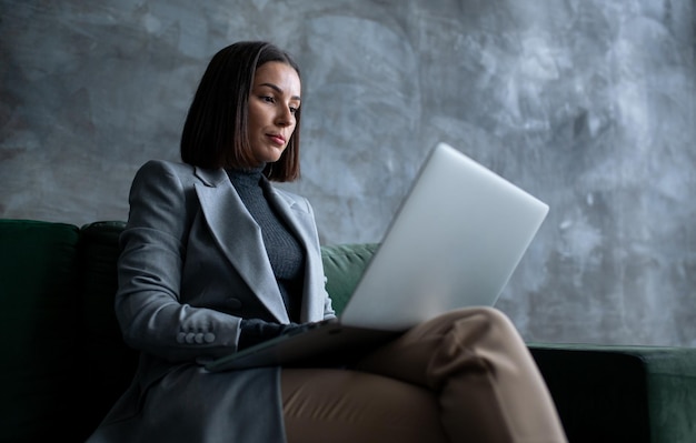 Jeune femme gestionnaire assise sur le canapé vert dans le salon du grenier et utilisant l'ordinateur femme créative