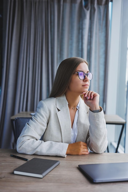 Une jeune femme gestionnaire réussie dans une élégante veste décontractée et des lunettes optiques est assise au bureau sur le lieu de travail une femme expérimentée avec un ordinateur portable moderne travaillant au bureau