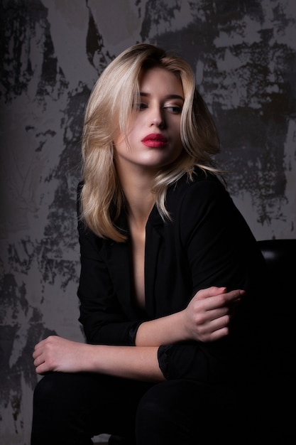 Jeune femme glamour aux lèvres roses portant une veste noire posant au studio avec des ombres