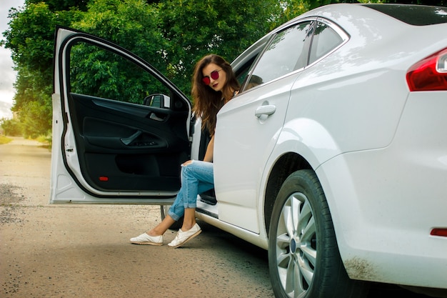 Jeune femme glamour avec des lunettes est assise dans une grande belle voiture blanche