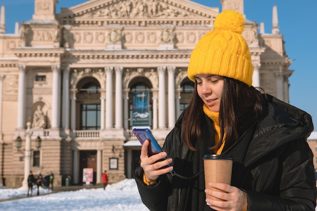 Jeune femme avec un gobelet jetable buvant du café l'opéra de lviv s'appuyant sur l'arrière-plan