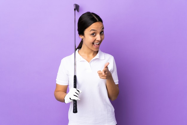 Jeune femme golfeur sur mur coloré surpris et pointant vers l'avant