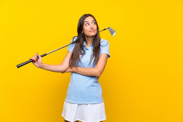 Jeune femme de golfeur sur mur jaune isolé faisant un geste de doutes tout en soulevant les épaules