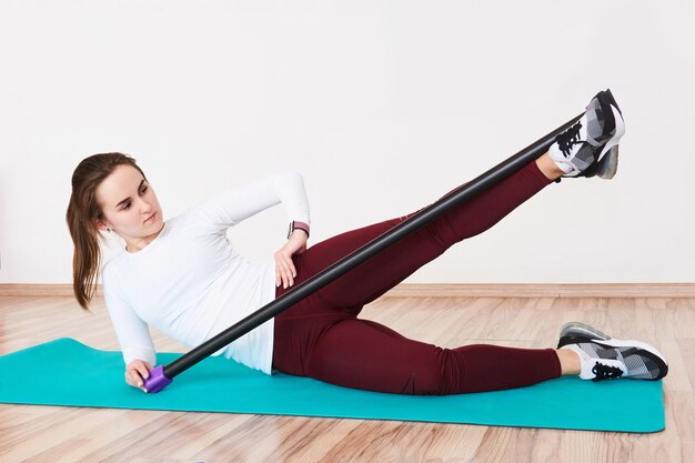 Une jeune femme gracieuse dans la salle de sport effectue un exercice de levée de cuisse extérieure avec une barre corporelle allongée