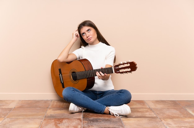 Jeune femme avec guitare assis sur le sol, ayant des doutes et avec une expression du visage confuse