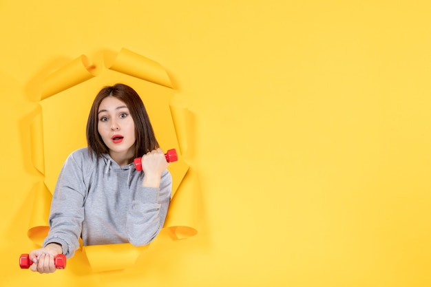 Jeune femme avec des haltères sur fond jaune athlète d'exercice fit gym