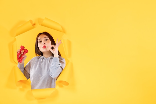 Jeune femme avec des haltères sur la surface jaune de l'athlète d'exercice de gym fit