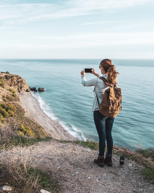 Jeune femme hanche avec un sac à dos explorant et photographiant la côte par une belle journée. Concept d'exploration et d'aventures