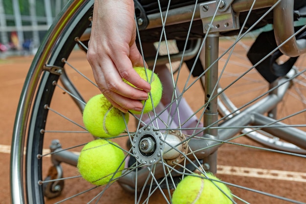 Jeune femme handicapée en fauteuil roulant jouant au tennis sur un court de tennis Libre d'une main prend une balle de tennis fixée dans une roue