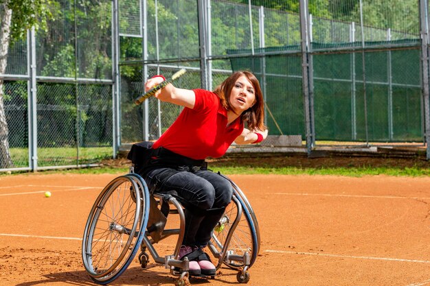 Photo jeune femme handicapée en fauteuil roulant jouant au tennis sur un court de tennis