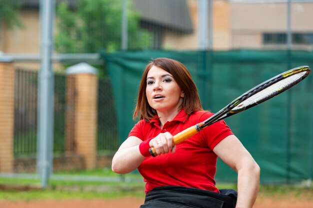 Jeune femme handicapée en fauteuil roulant jouant au tennis sur un court de tennis.