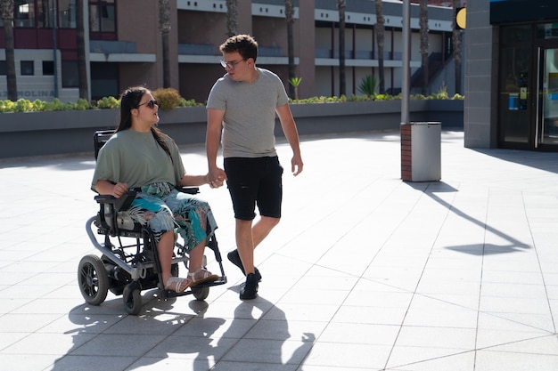 Jeune femme handicapée en fauteuil roulant et son petit ami aimant ou son mari se tenant la main et se regardant