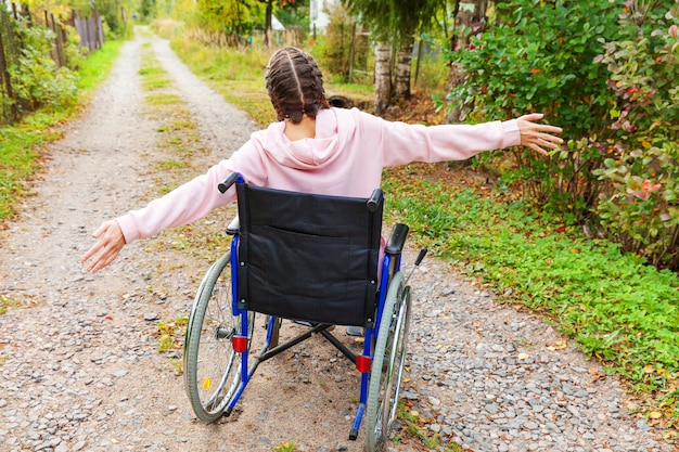 Jeune Femme Handicapée Heureuse En Fauteuil Roulant Sur La Route Dans Le Parc De L'hôpital Jouissant De La Liberté. Fille Paralysée Dans Une Chaise Invalide Pour Les Personnes Handicapées En Plein Air Dans La Nature. Concept De Réadaptation.