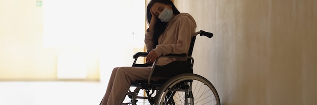 Jeune Femme Handicapée Portant Un Masque Médical De Protection Assise En Fauteuil Roulant Dans Le Couloir De L'hôpital