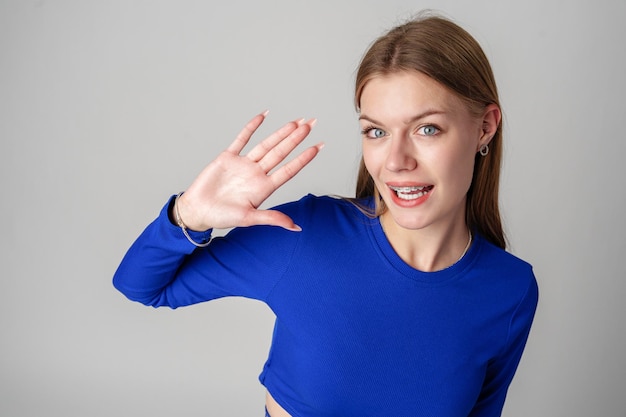 Une jeune femme en haut bleu fait un geste de main.