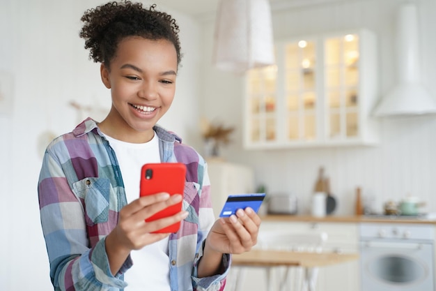 Une jeune femme heureuse achète en ligne avec un téléphone portable et une carte de crédit