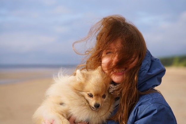 Une jeune femme heureuse ou une adolescente marchant avec son chien spitz poméranien sur la plage tient un chiot