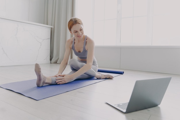Jeune femme heureuse adulte appréciant le yoga pratiquant l'étirement asana par leçon en ligne