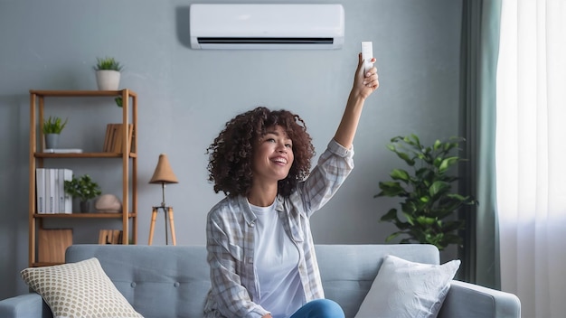 Jeune femme heureuse assise sur le canapé sous le climatiseur et réglant la température de confort avec rem