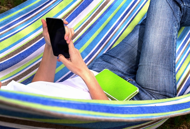 Une jeune femme heureuse assise dans un parc sur l'herbe verte dans la nature avec un téléphone dans ses mains dans des vêtements décontractés et discutant par lien vidéo le concept de méditation récréative saine