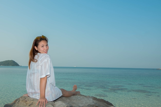 Jeune femme heureuse assise sur le rocher à la plage