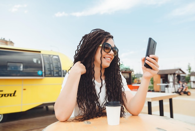 Une jeune femme heureuse assistant à une conférence Web via des écouteurs ou un pigiste assis à une table de café en plein air une fille avec des dreadlocks communique via un lien vidéo