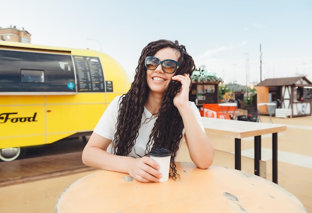 Une jeune femme heureuse assistant à une conférence Web via des écouteurs ou un pigiste assis à une table de café en plein air une fille avec des dreadlocks communique via un lien vidéo