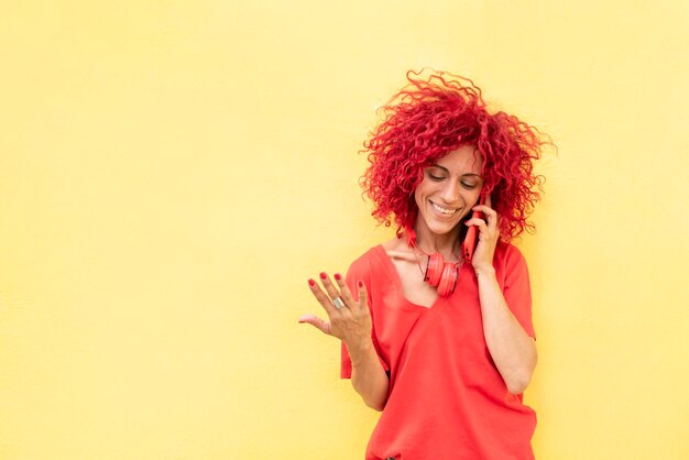 Une jeune femme heureuse aux cheveux afro rouges parle sur le smartphone sur fond jaune