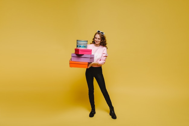 Une jeune femme heureuse avec des boîtes en papier coloré après le shopping isolé sur un fond orange Studio