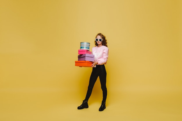 Une jeune femme heureuse avec des boîtes en papier colorées après le shopping isolée sur un fond orange Studio. Ventes saisonnières, achats, dépenses en cadeaux
