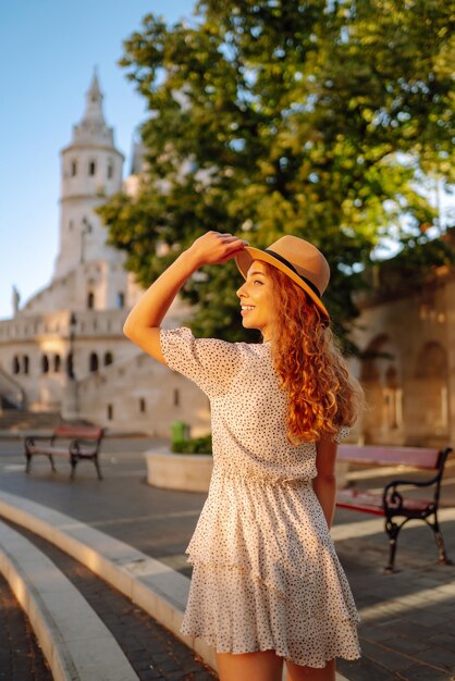 Une jeune femme heureuse avec un chapeau à l'aube profite de la vue sur de beaux bâtiments Concept de loisirs de style de vie