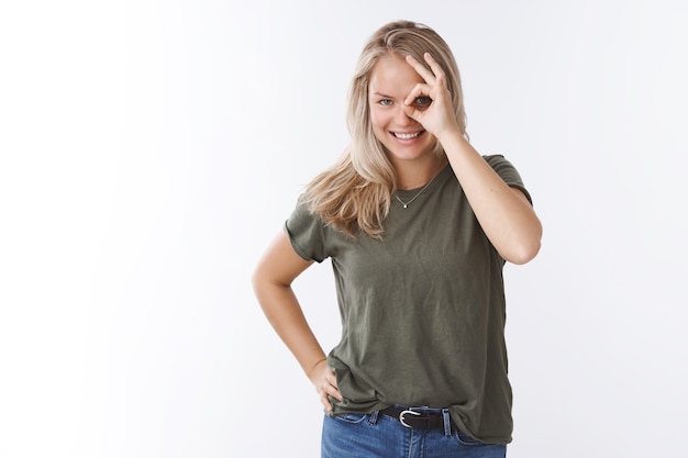 Jeune Femme Heureuse Charismatique Aux Cheveux Blonds Et Aux Yeux Bleus Regardant à Travers Le Trou Montrant Un Geste Correct Sur Les Yeux Et Regardant La Caméra Amusée Et Joyeuse Souriante Effrontée Sur Fond Blanc