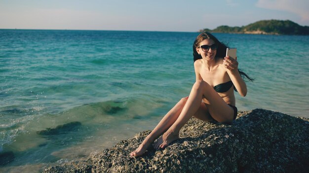 Jeune femme heureuse discutant avec des amis via Internet à l'aide d'un smartphone sur la plage de l'océan