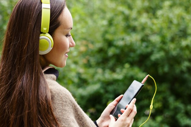 Jeune femme heureuse écoute de la musique de smartphone avec un casque dans un parc calme