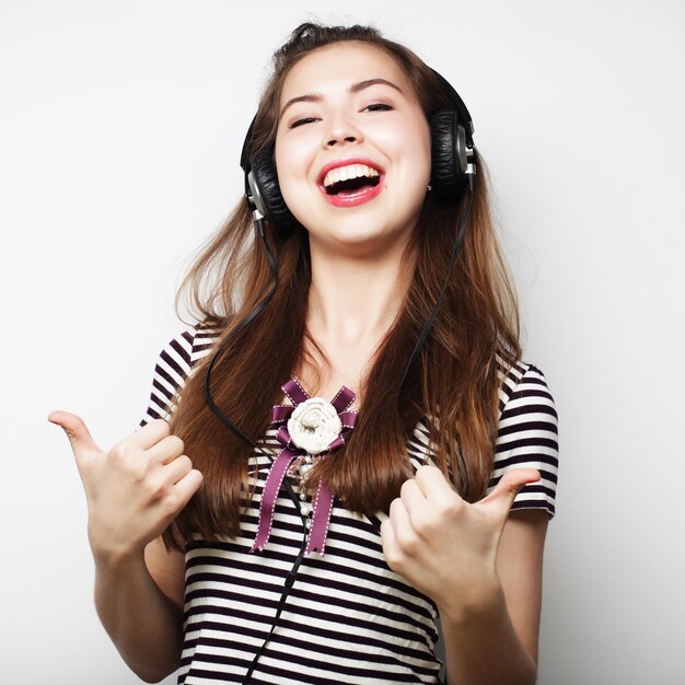 Jeune femme heureuse avec des écouteurs écoutant de la musique sur fond gris