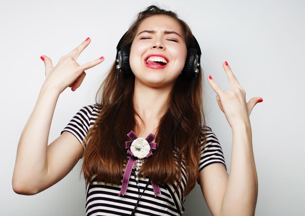 Jeune femme heureuse avec des écouteurs écoutant de la musique sur fond gris