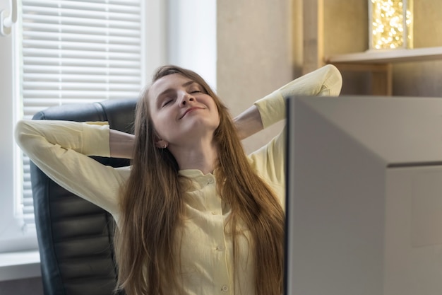 Une jeune femme heureuse est assise les yeux fermés et a joint ses mains derrière sa tête. Repos du travail