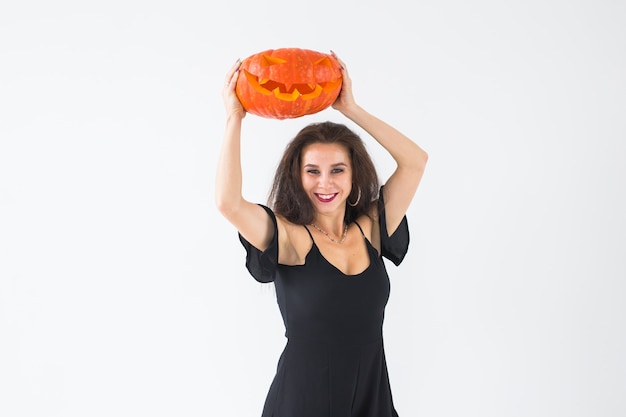 Jeune femme heureuse excitée en costume d'halloween posant avec une citrouille sculptée sur fond clair avec espace de copie